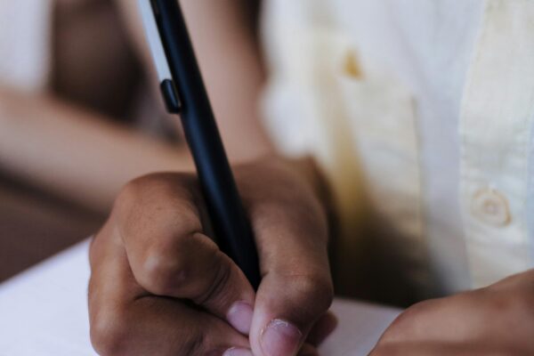 Child's hands writing with a pen on paper indoors, showing focus and concentration.